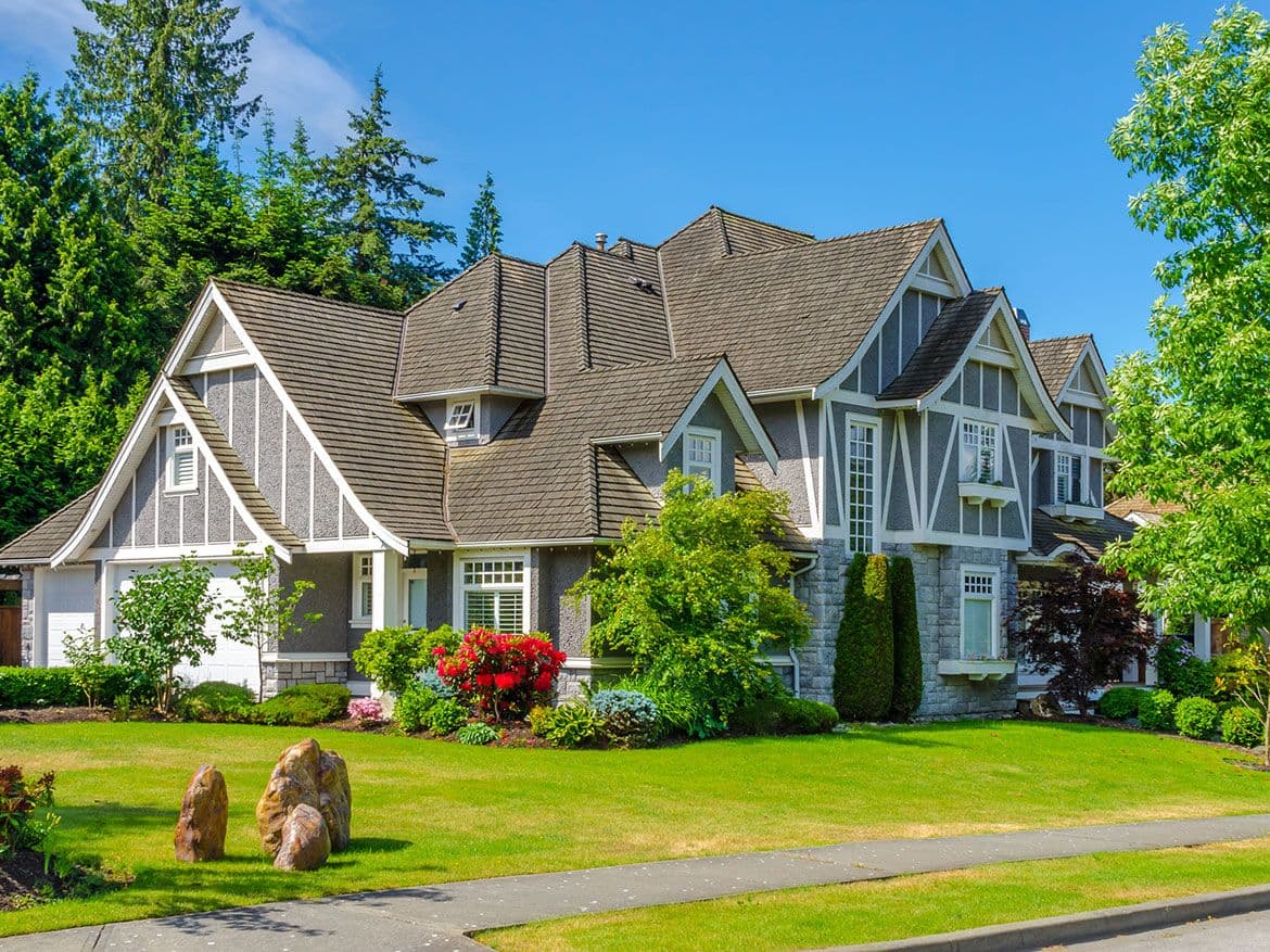 Large gabled house with a stone base, flower beds and a green lawn